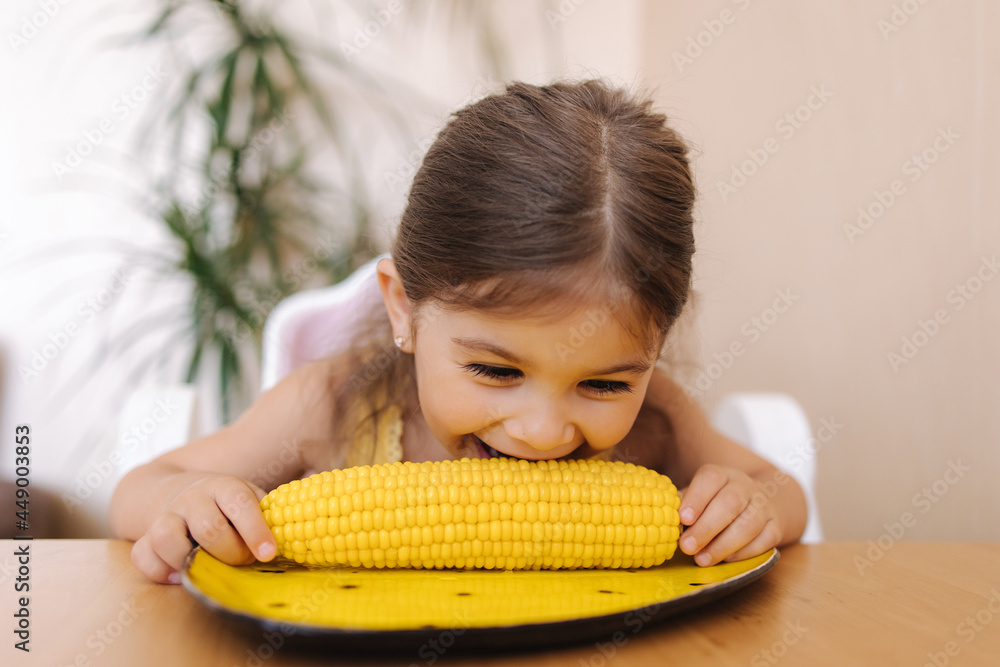 Adorable little girl eating corn at home. Cute kid tree year old eat boild corn