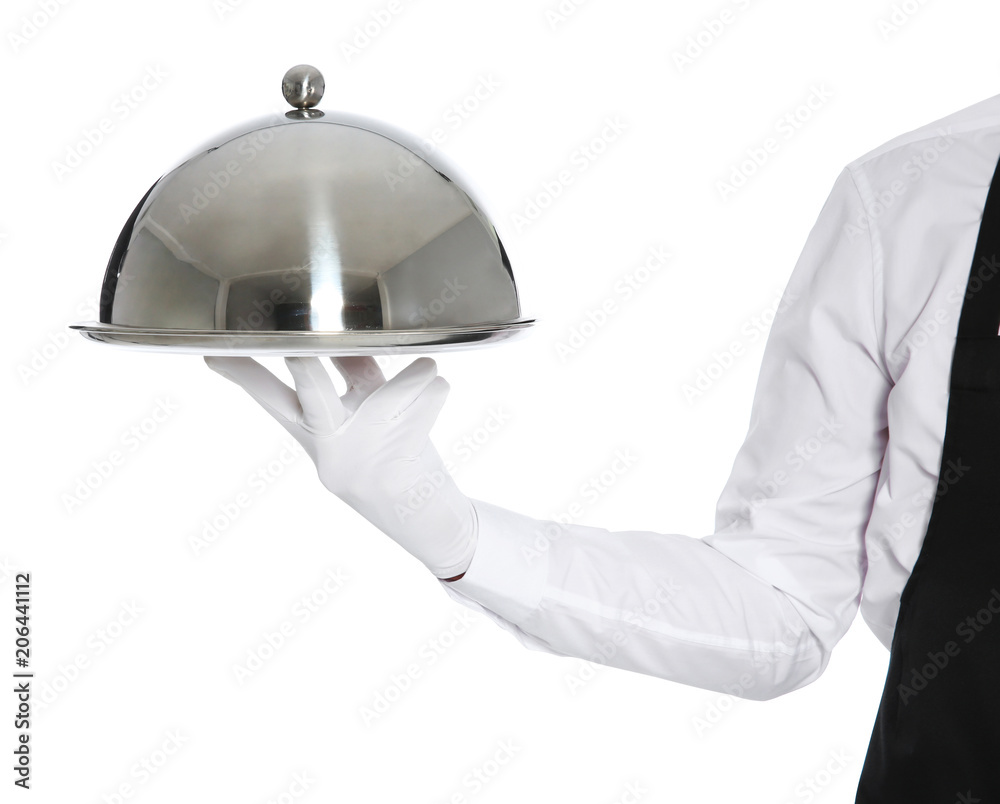 Young waiter holding metal tray with lid on white background