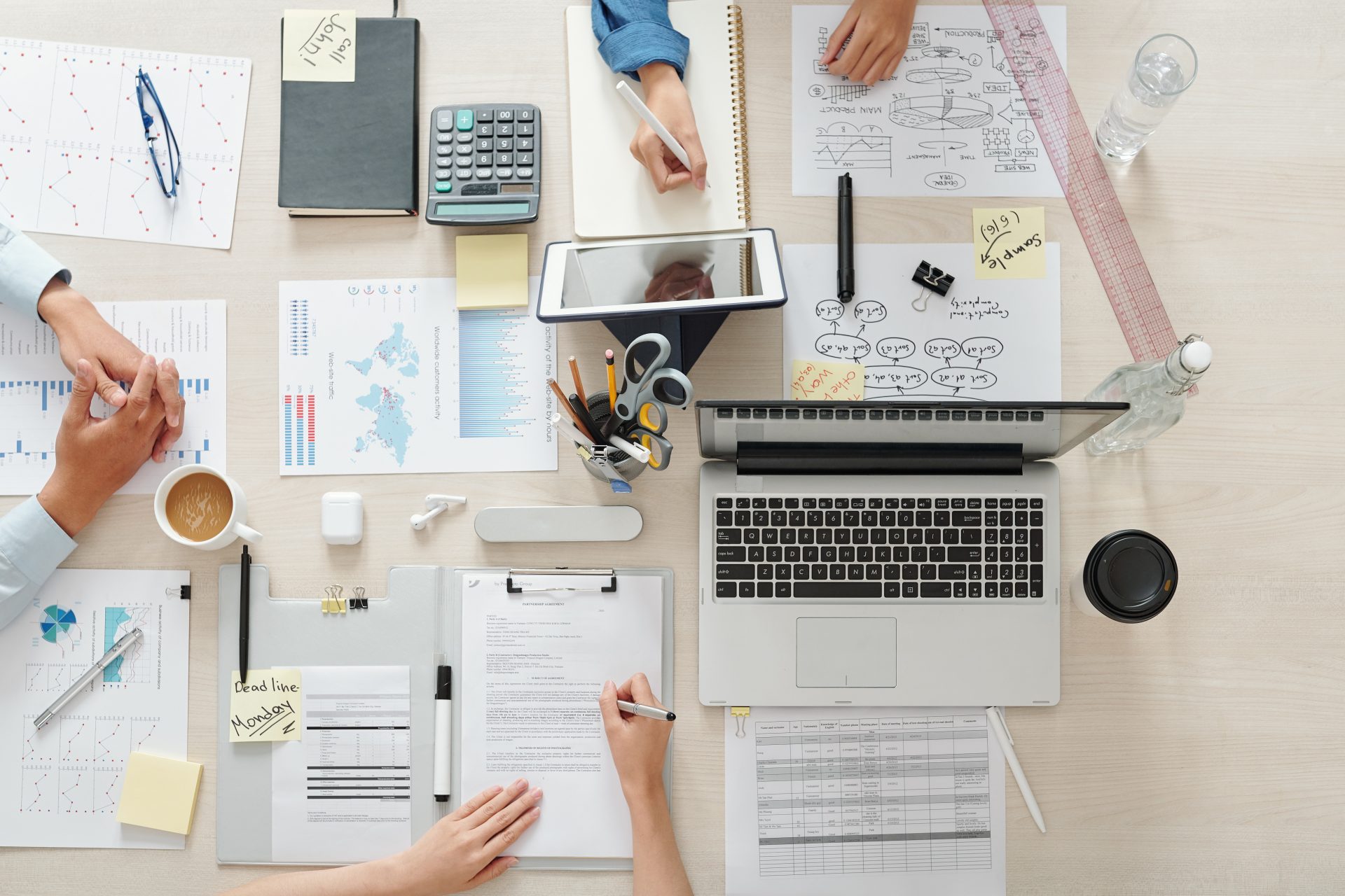 Marketing team working on project at table with charts, documents and gadgets, view from the top