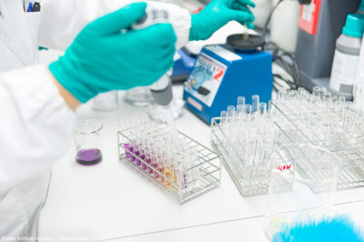 A gloved hand injects fluid into a test tube.