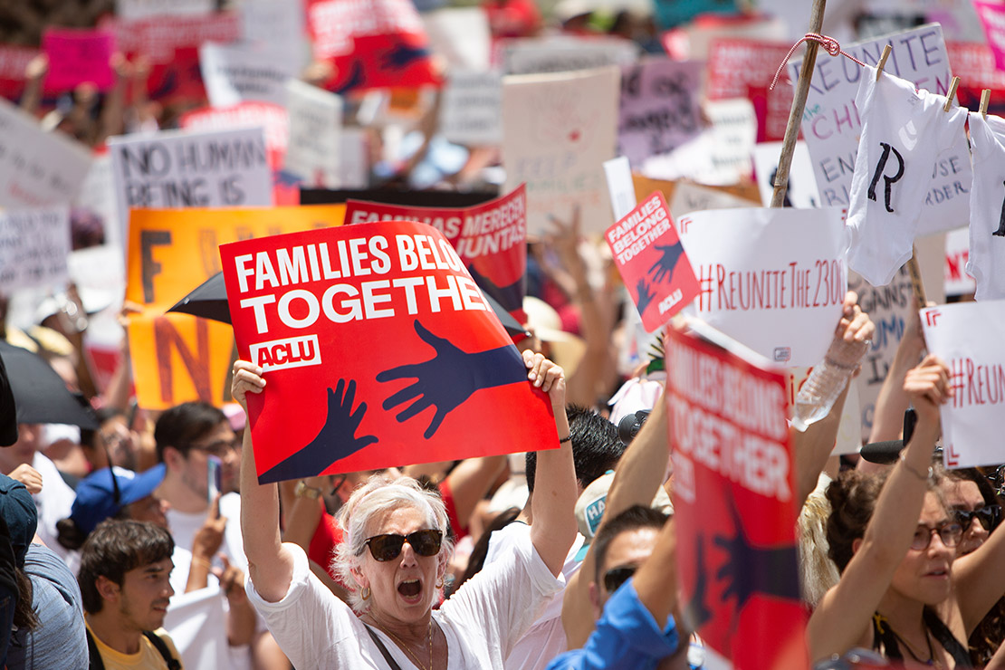 Demonstrators hold signs, one of which says "Families Belong Together."