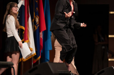 Cecilia Bartin jumping on stage in "Girls State," now streaming on Apple TV+.