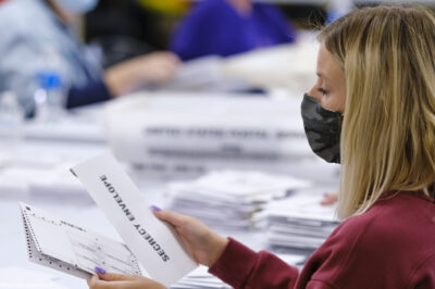 A woman with a surgical mask opening absentee ballots.