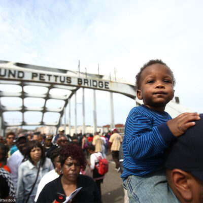 An infant sits atop His Father's Shoulders As Marchers Cross the Edmund Pettus Bridge During the 50th Anniversary Commemoration of the 'Bloody Sunday' Crossing of the Bridge in Selma Alabama.