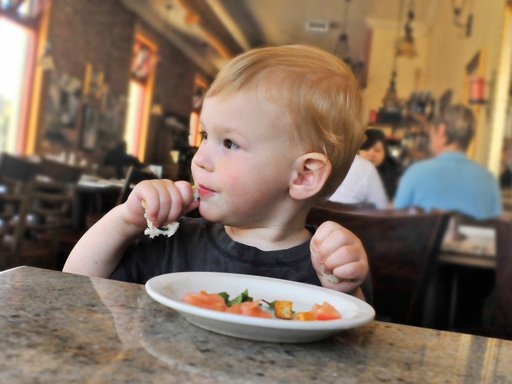 Toddler boy eating salad at restaurant