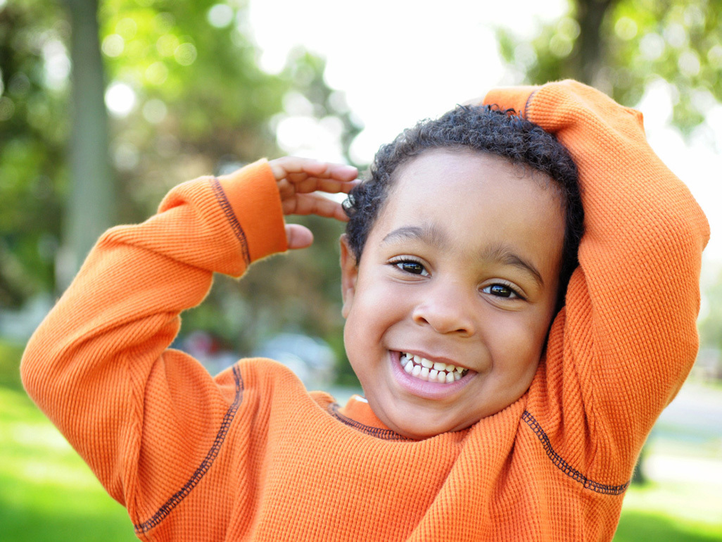 young boy in orange shirt with hands above his head smiling outdoor