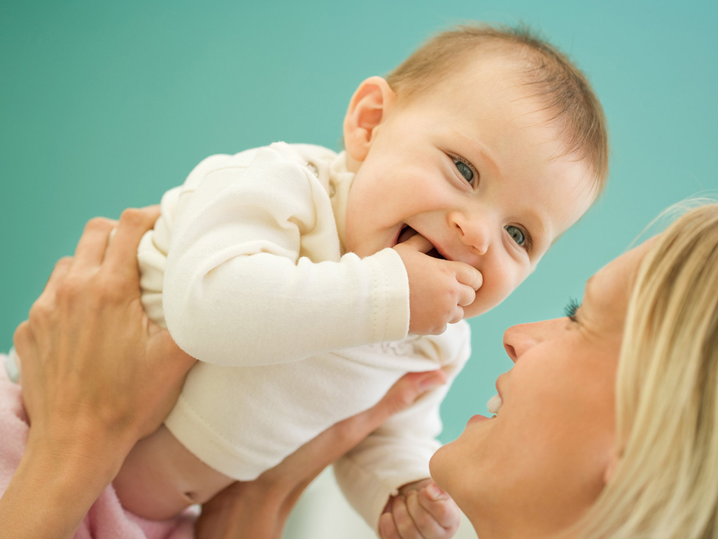 Mother lifting up laughing baby with fingers in mouth