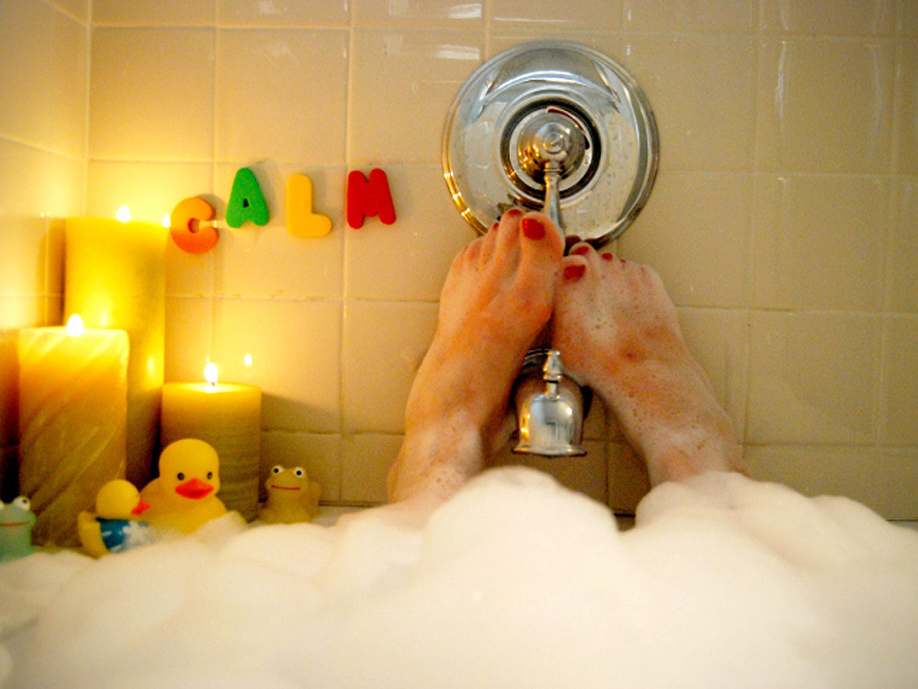 Woman relaxing in a bubble bath with candles.The word "calm" is written on the tiles