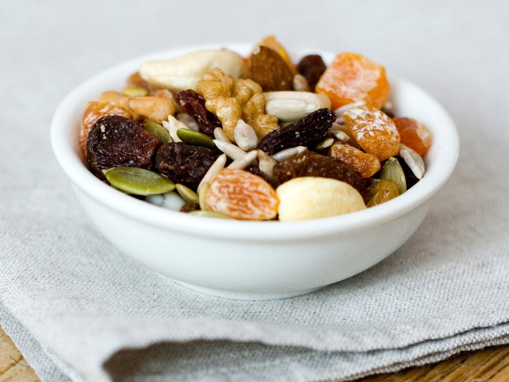 small white bowl full of walnuts, raw cashews, seeds and dried fruit