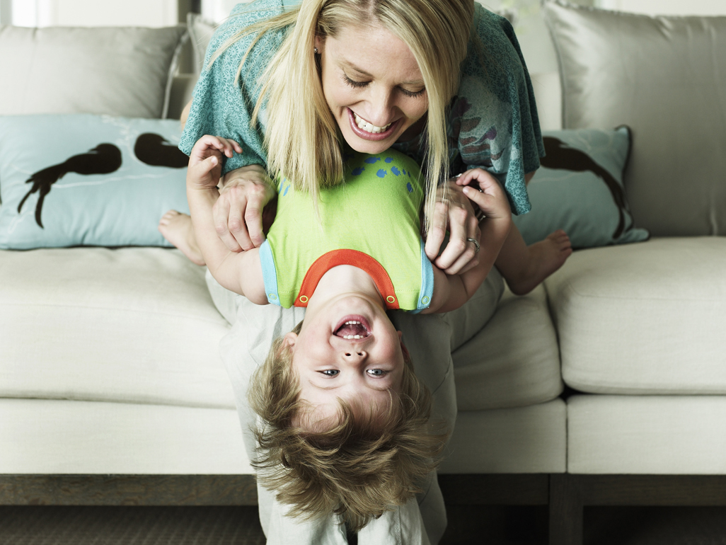 child leaning off couch, being held by mom