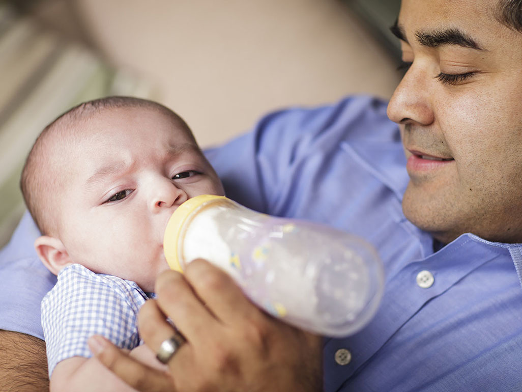 man holding a baby and a bottle, while baby is drinking from the bottle