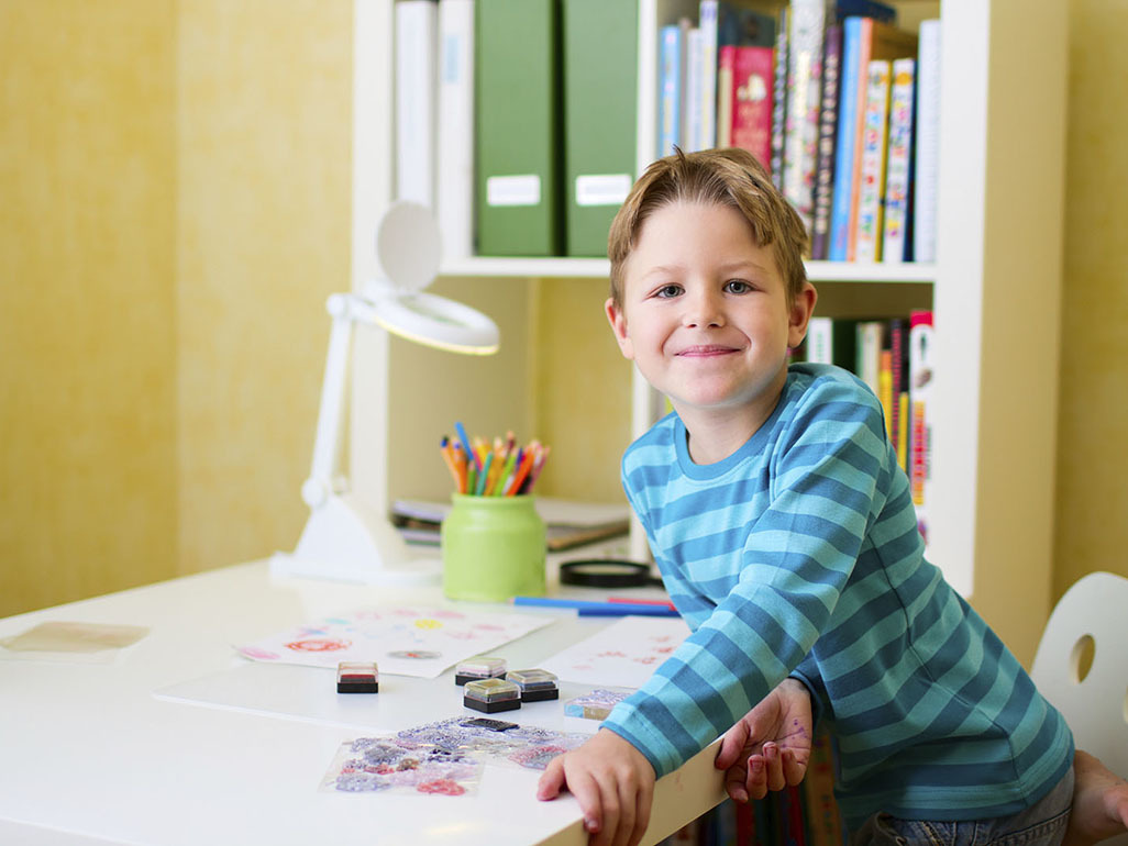 boy sitting at the desk with some crayons and drawings in front of him