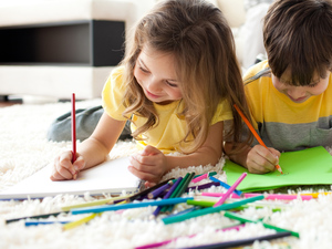 two kids drawing with wooden crayon on papers