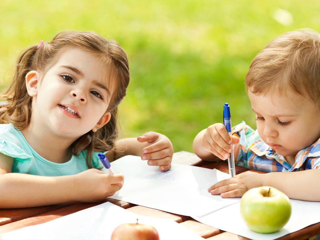 two kids sitting outside and writing on paper