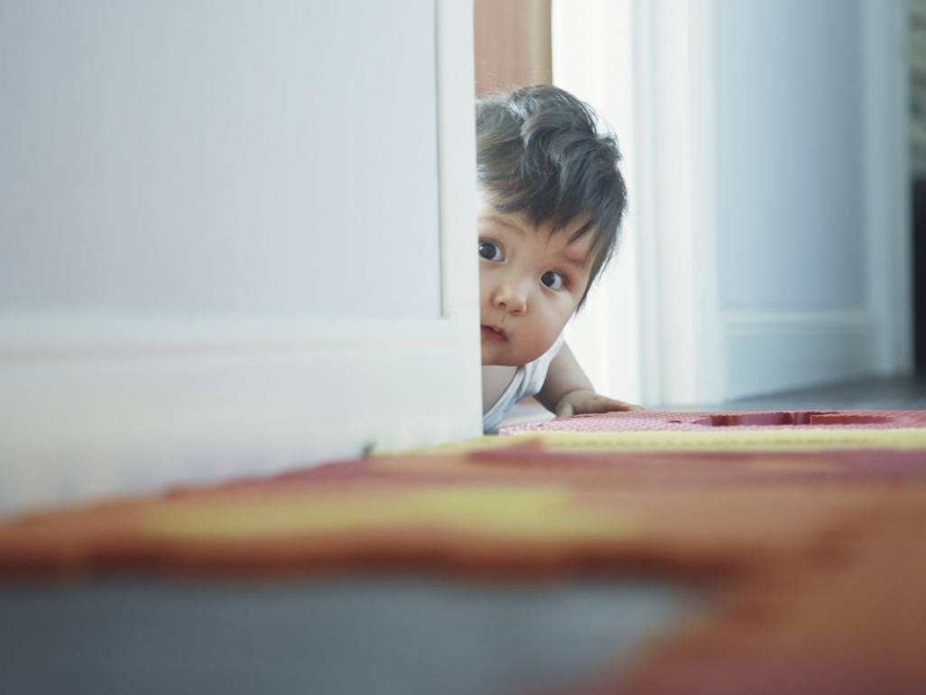 crawling baby with a face half hidden behind the corner looking at something very curiously