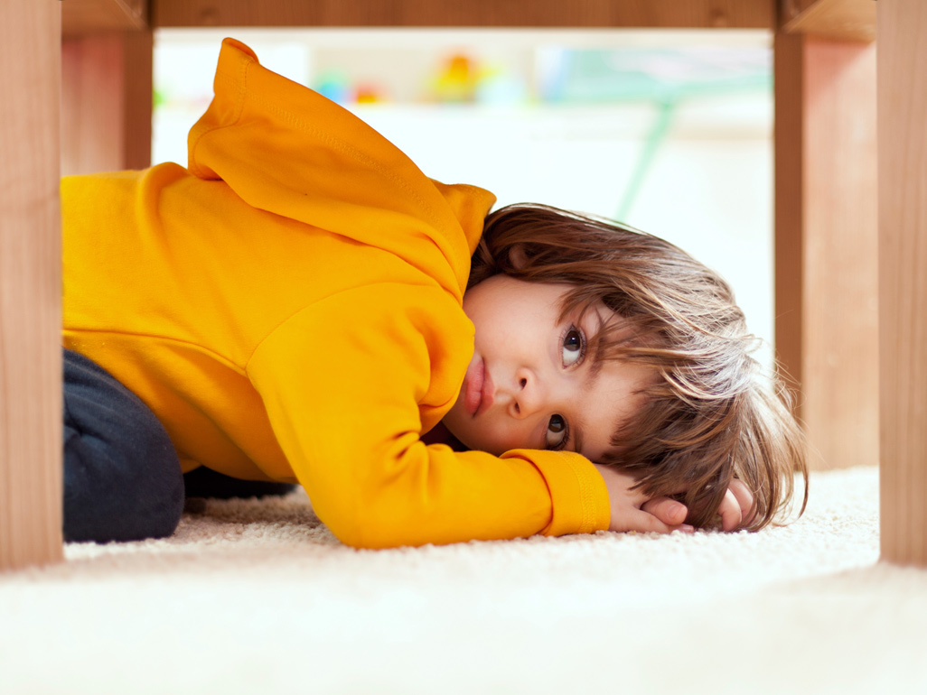 child wearing a hoodie hiding under a table