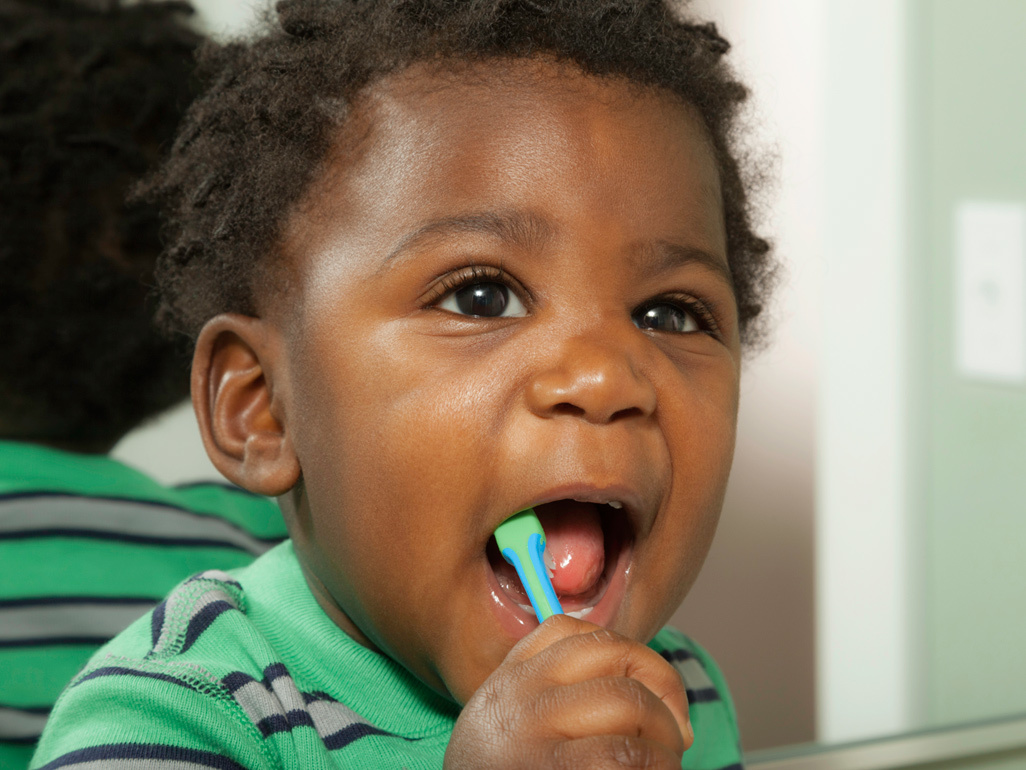 baby with curly hair brushing it's teeth