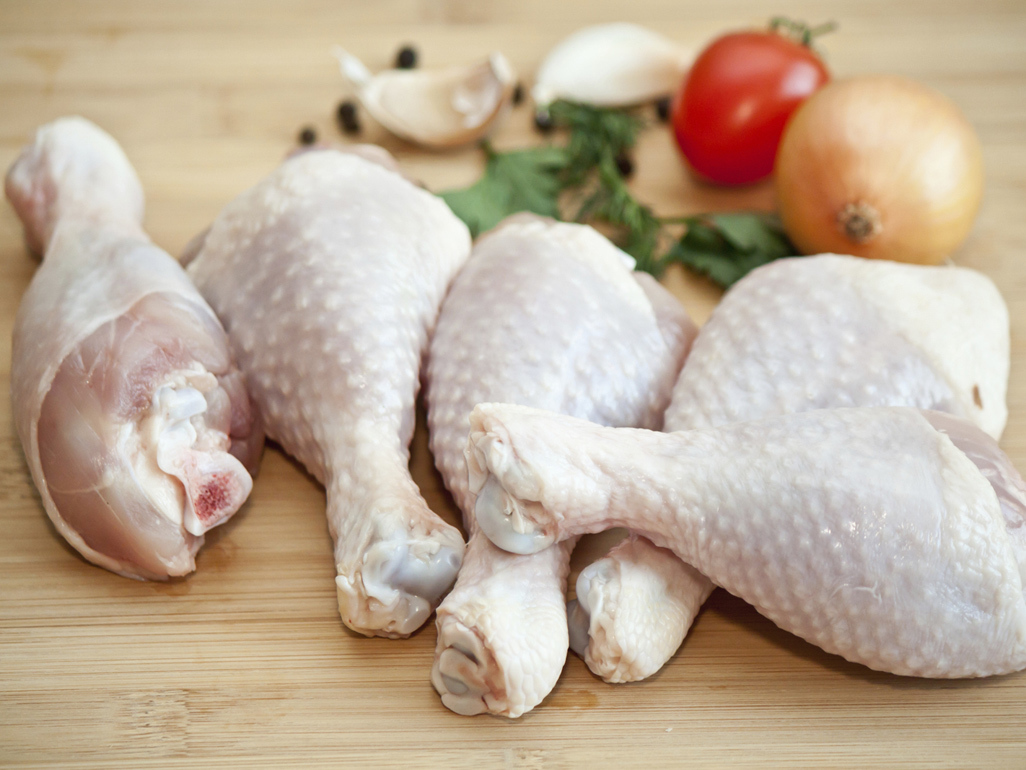 raw chicken drumsticks on wooden board with herbs, garlic onion and tomato