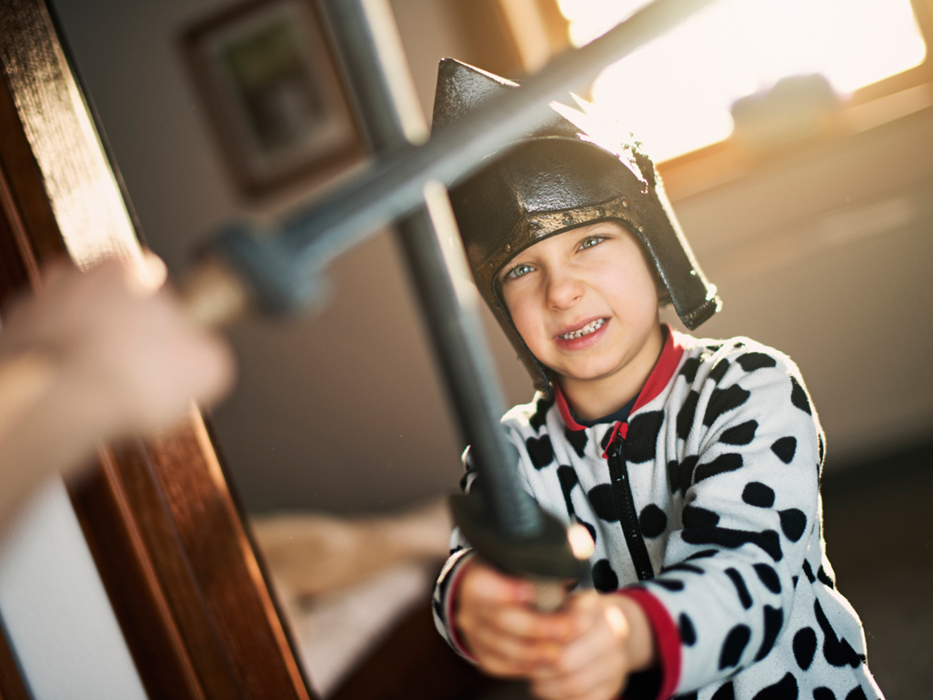 child with a helmet on his head sword fighting with another person using a bokken