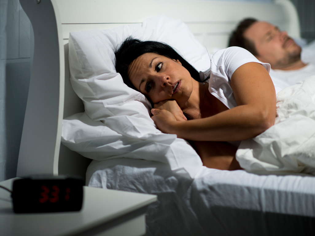 Woman lying awake in bed next to sleeping man