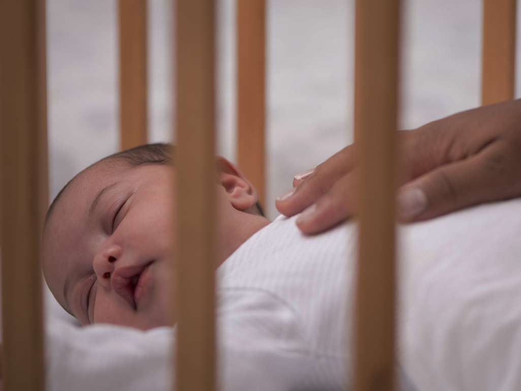 An adult resting their hand on a baby's chest while the baby sleeps