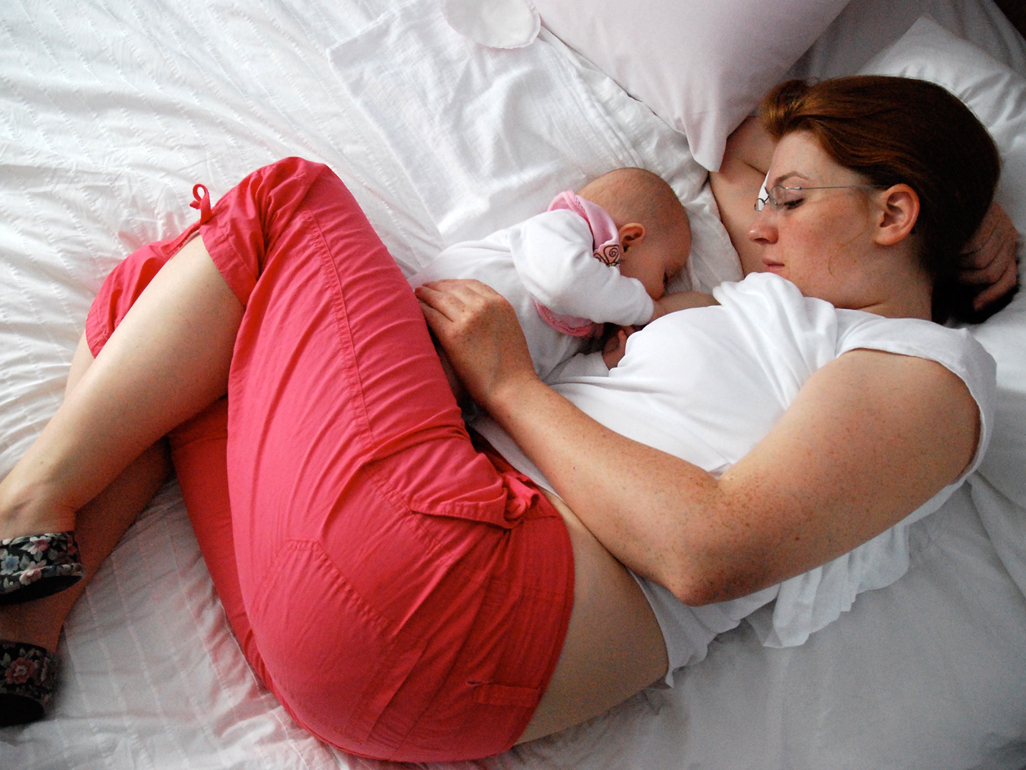 Mum lying on bed breastfeeding newborn baby