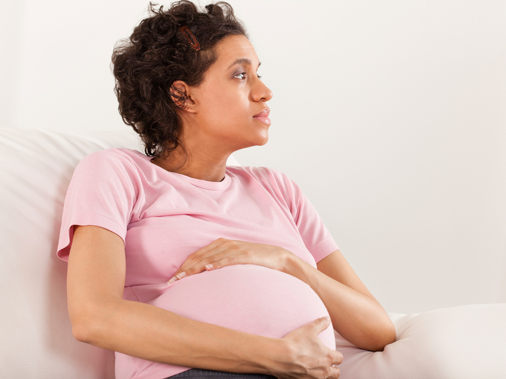 Woman sitting down, cradling her bump and looking worried