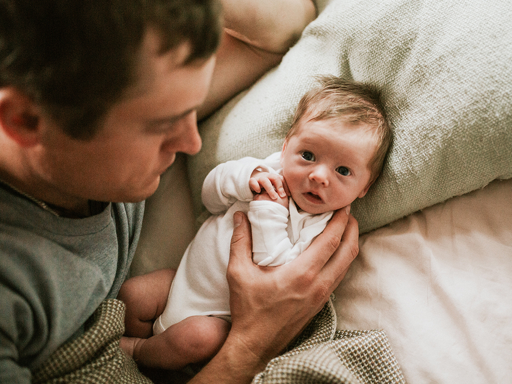 Dad lying on bed with newborn