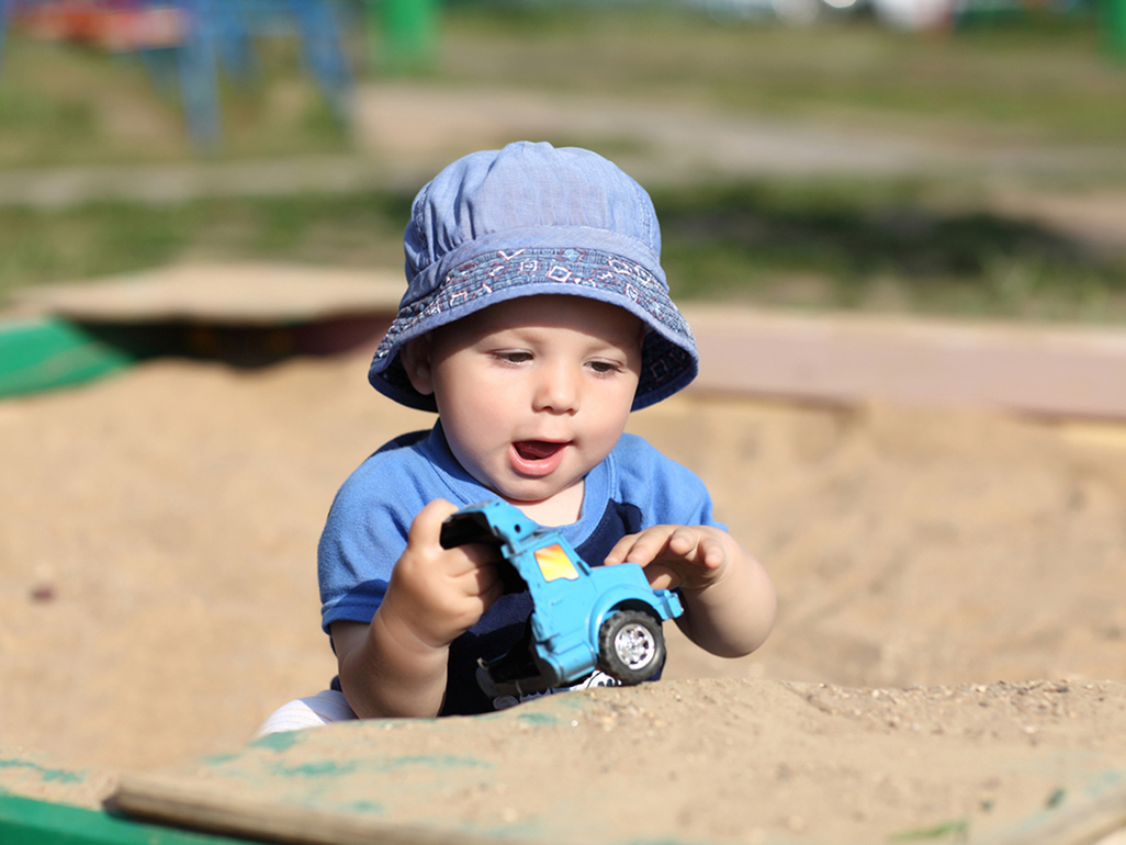 boy in blue hat holding a truck, sitting in sand