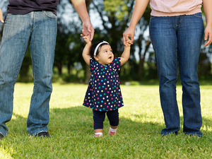 Toddler learning to walk holding her parents hands