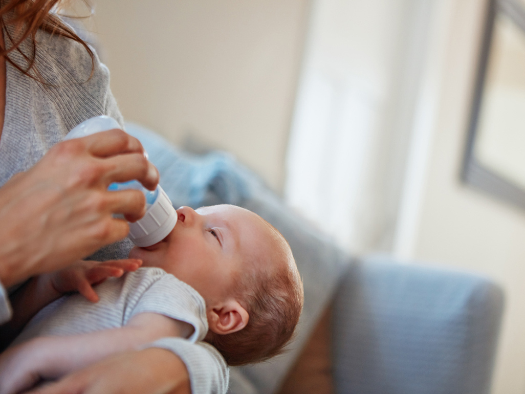 A mom bottle feeding a newborn baby at home.