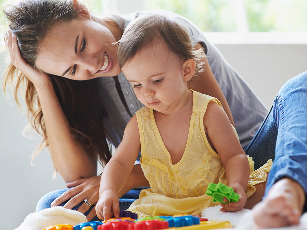 woman sitting next to a baby girl who is playing with various play shapes