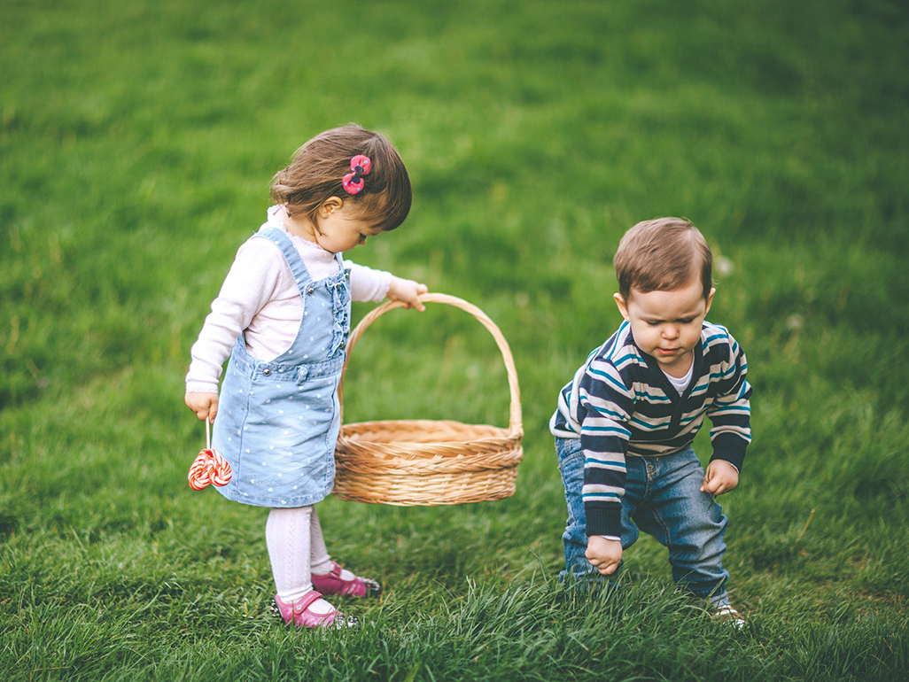 little girl holding a basket while little boy picks grass