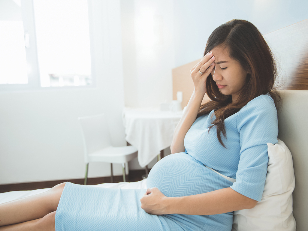 A pregnant woman clearly in pain, resting on the bed with one hand on her forehead.