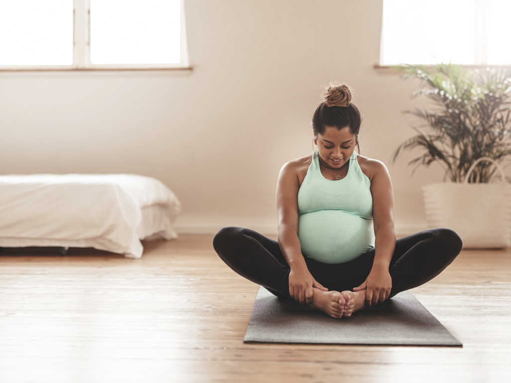 Pregnant woman doing yoga at home wearing maternity leggings