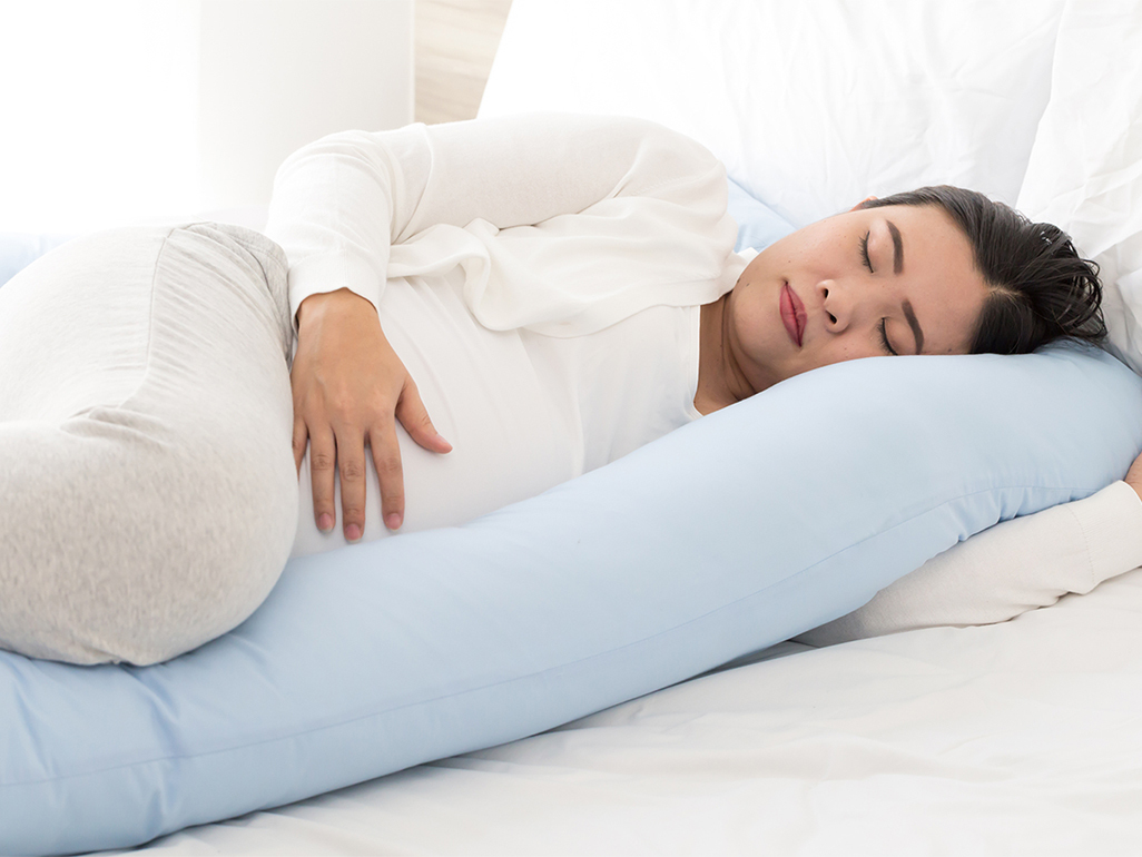 Woman sleeping on bed cuddling pregnancy pillow