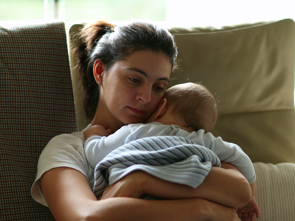 tired new mom sitting on the couch holding her baby