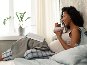 Pregnant woman reading a book laying on her bed