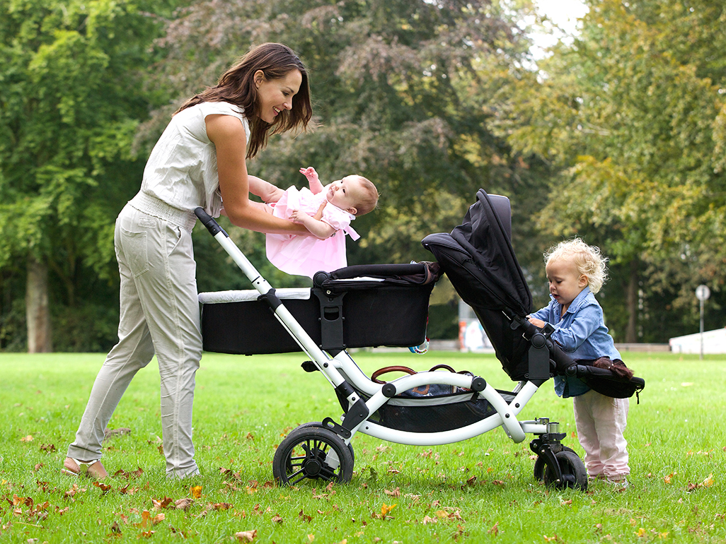 Mum putting her baby into a double buggy with another child alongside