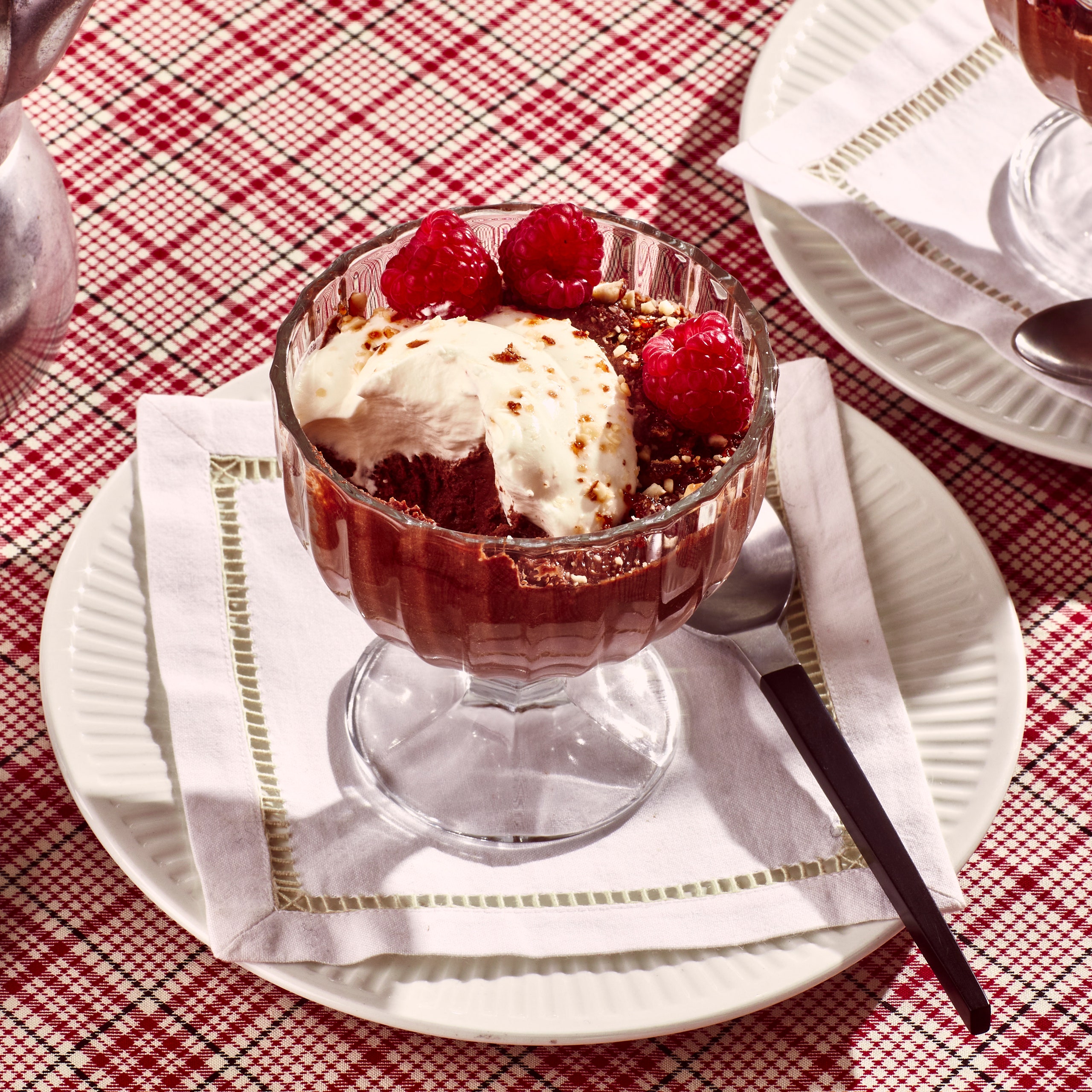 Two glass dessert cups filled with chocolate pudding topped with whipped cream almond praline and raspberries.