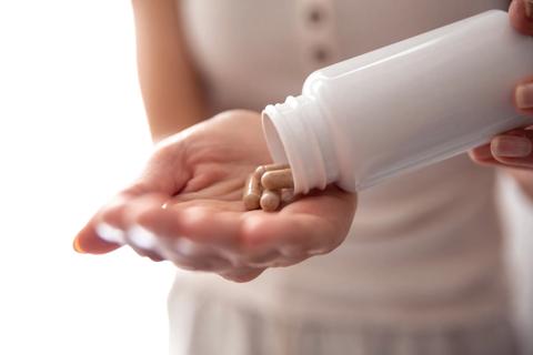 Hand pouring capsules out of white bottle into other hand