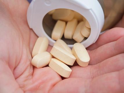 Tan tablets pouring from bottle into a hand