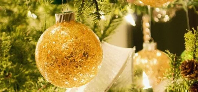 Gold Christmas ornament hanging on a green tree branch.