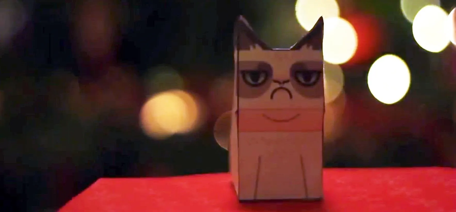 Paper cat figure in front of blurred festive lights.