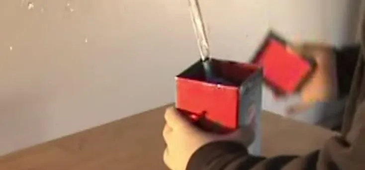 A person pouring liquid into a red container on a table.