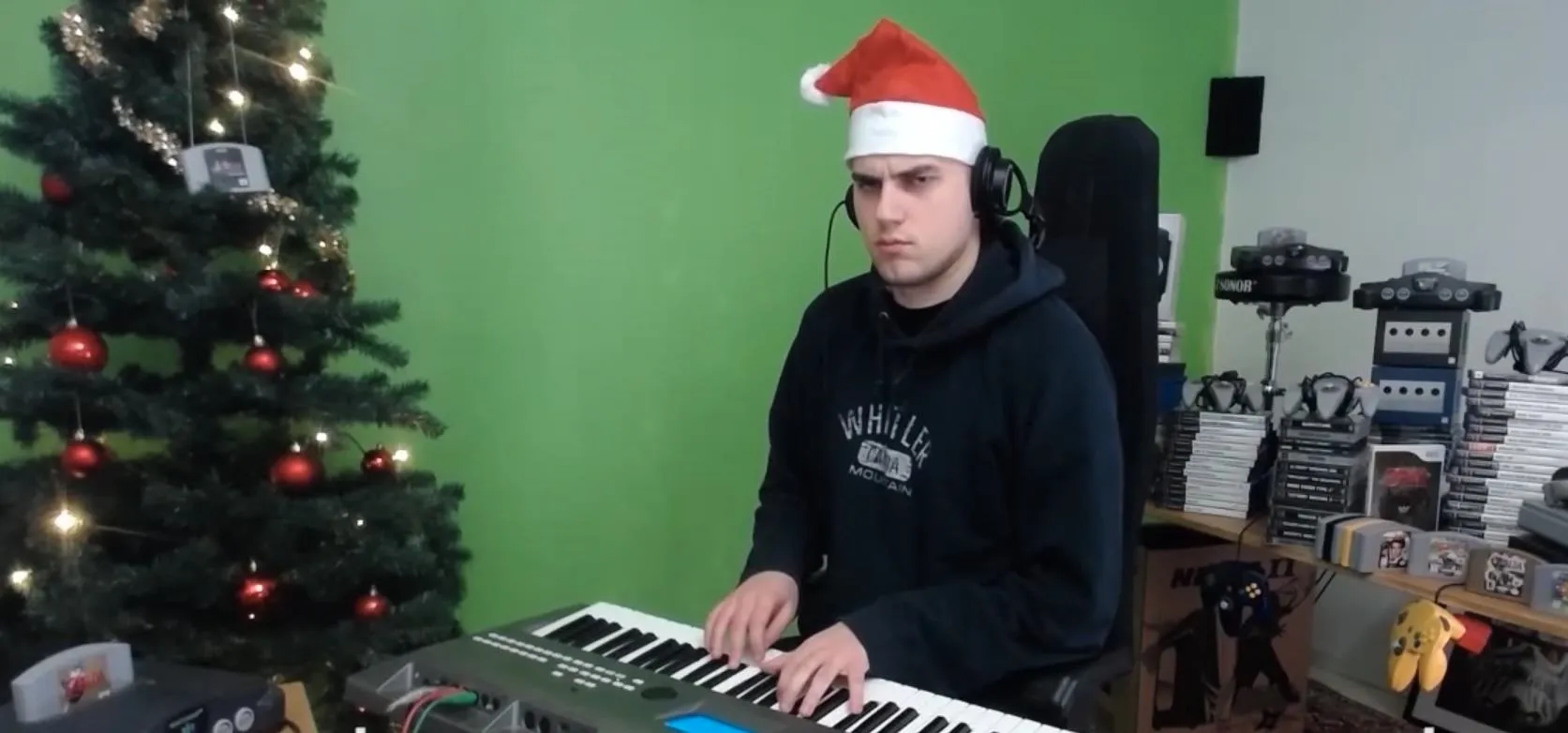 Person wearing a Santa hat playing a keyboard in front of a decorated Christmas tree.