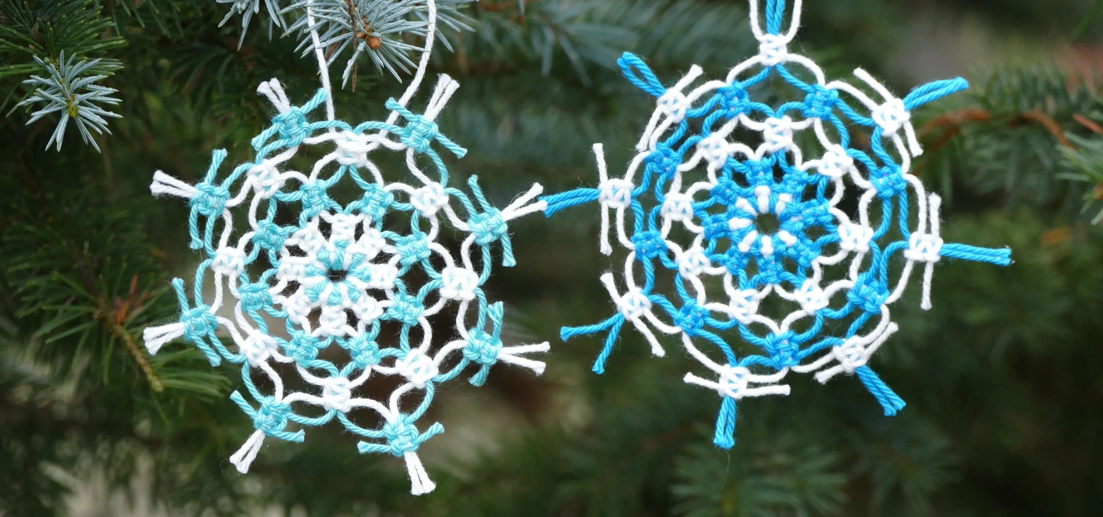 Delicate handcrafted snowflake ornaments in blue and white hang from evergreen branches.