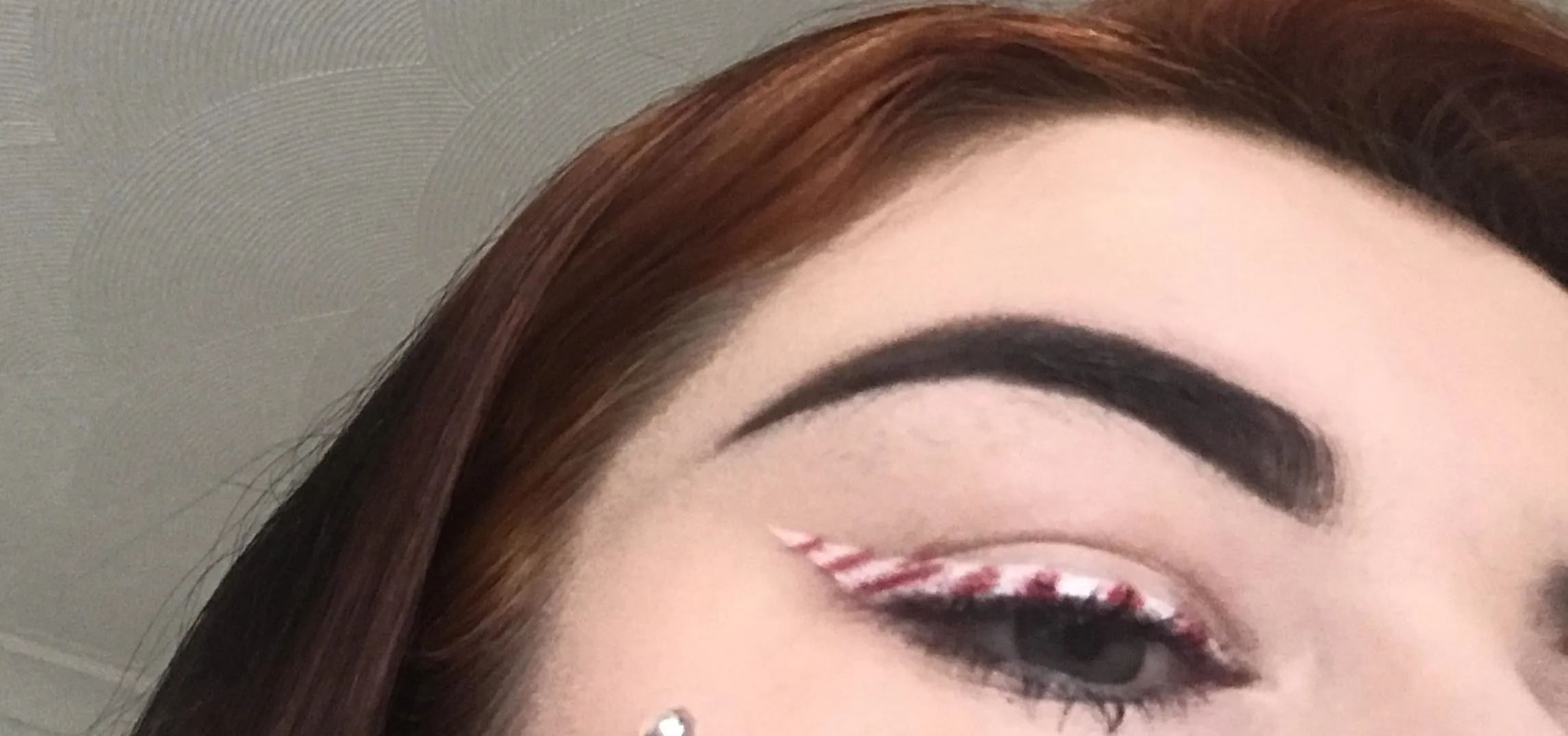 Close-up of an eye with festive makeup featuring red and white striped eyeliner and well-defined eyebrows.