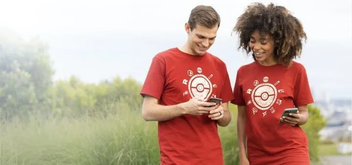 Two people in red shirts looking at their smartphones while walking outdoors.