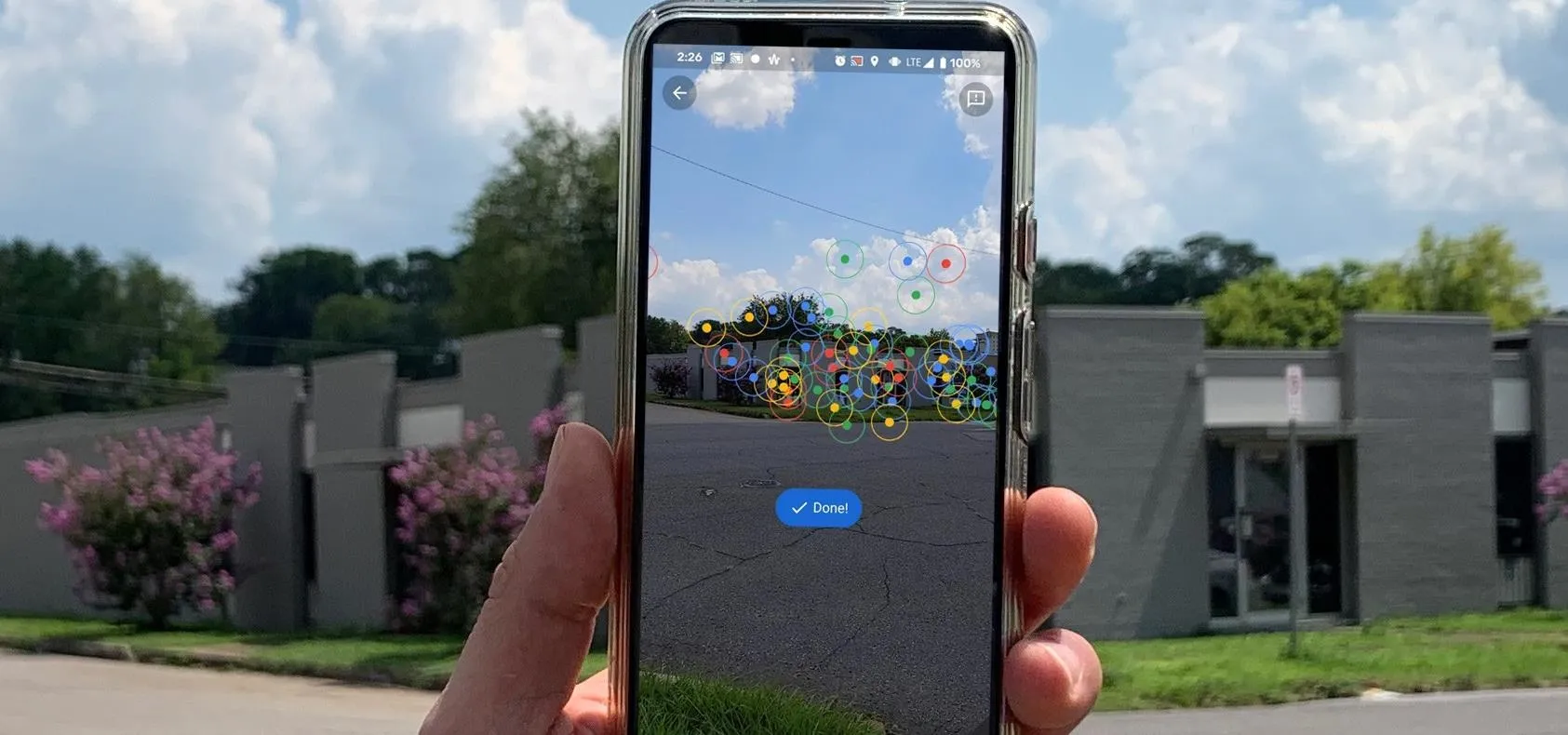 Person holding a smartphone displaying an augmented reality application with a view of a cloudy sky and buildings in the background.